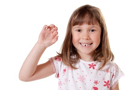 A smiling young girl holds a tooth between her fingers